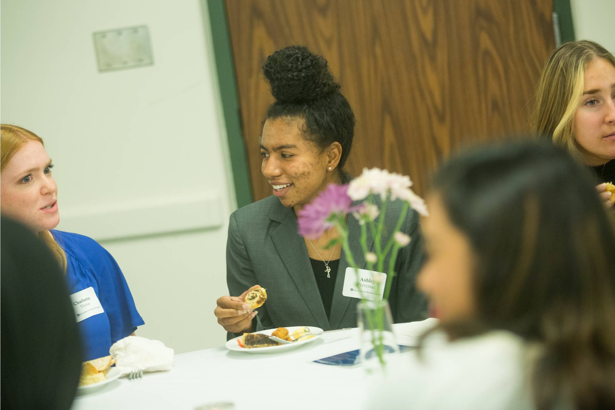 student speaking with another student at a table